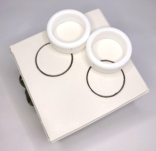Two white 4 to 50mm Double Flared Tunnel Moulds by The Cerulean Wolf are displayed on a white square surface above matching black-outlined circles, highlighting their clean, circular design in a visually aligned arrangement.