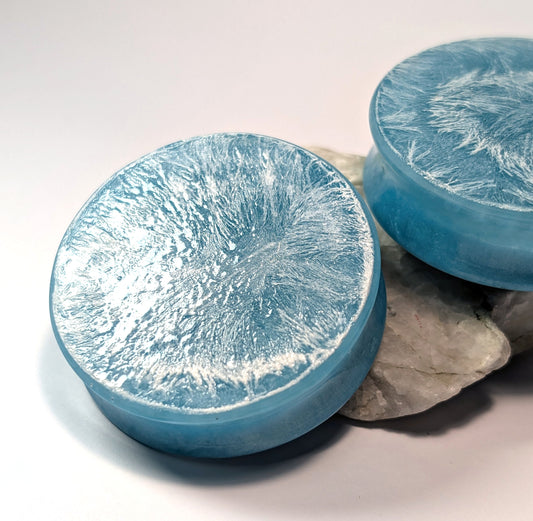 Two light blue double flared, stretched ear plugs with a white textured surface on a white background