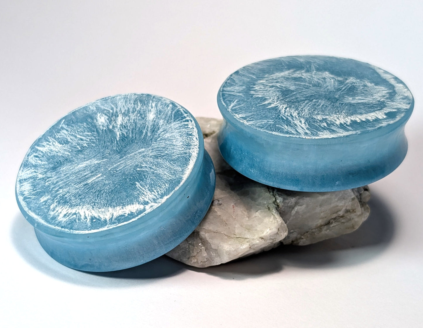 Two light blue double flared, stretched ear plugs with a white textured surface on a white background