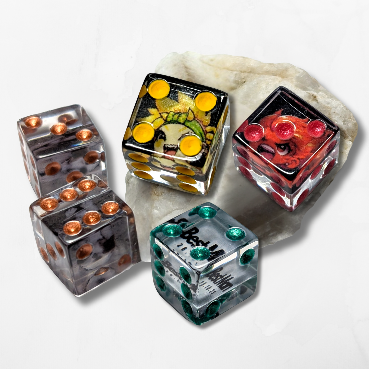 Five Custom Photograph Pipped D6 dice by The Cerulean Wolf, each with colored pips (yellow, red, orange, green, brown), sit on a white stone. Two novelty gift dice display cartoon faces or designs. White background.