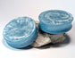 Two light blue double flared, stretched ear plugs with a white textured surface on a white background